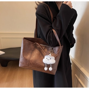 Detail of a large brown contrast tote bag with a white plush cloud charm and retro texture