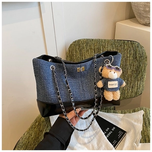 Detail of blue denim tote bag with black patent leather bottom and bear charm on green chair