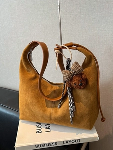 Retro brown suede hobo bag with teddy bear pendant and ribbon detail on white book