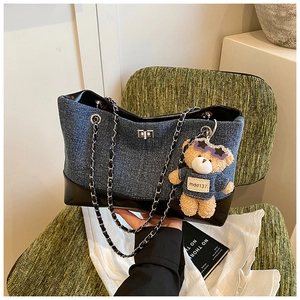 Detail of denim tote bag with silver twist lock, chain strap and a cute teddy charm