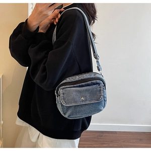 Detail of blue denim square crossbody bag with silver buckle worn on person