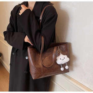 Detail of vintage brown textured leather tote bag with logo and cute cloud plush charm