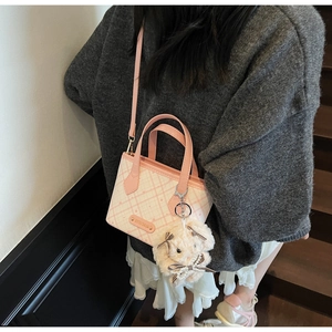 Detail of pink checkerboard tote bag with plush bear charm and brand logo tag
