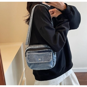Detail of blue denim crossbody bag featuring a front pocket and wide shoulder strap