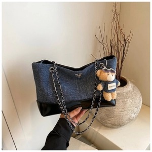 Detail of blue denim tote bag featuring black leather trim and cute teddy bear charm
