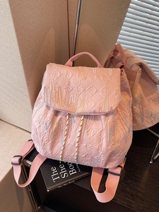 Pink quilted backpack with textured fabric and wavy colorful embroidery shown via a mirror