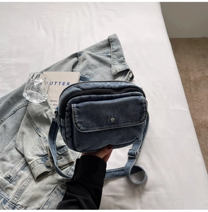 Detail of blue denim crossbody bag with multiple zipper compartments and metal buckles