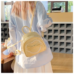 Détail d'un mini sac à dos jaune clair avec cœur en dentelle et nœud porté par un mannequin