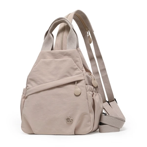 Detail of nylon sling bag showing front diagonal zip and circular logo on beige fabric