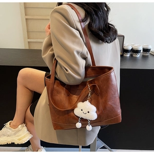 Detailed view of a brown vintage tote bag with a white fluffy cloud pendant charm