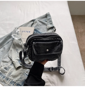 Detail of black denim crossbody bag featuring multi-zipper layers and adjustable strap