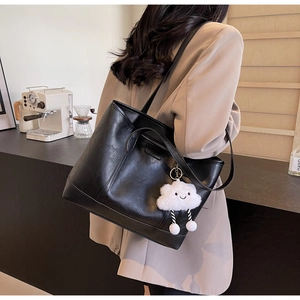 Detail of black faux leather tote bag with white cloud plush charm on a slim shoulder strap