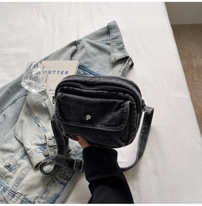 Close-up of black washed denim crossbody bag texture with functional front flap pocket