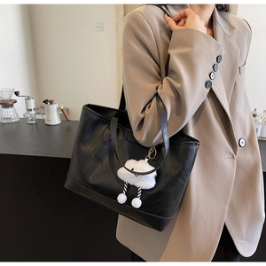Black leather tote bag with white cloud plush charm shown in a coffee shop setting