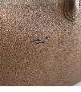 Gros plan sur un sac cabas en cuir marron grainé montrant les poignées et le logo gravé