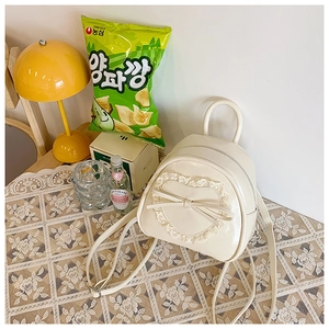 Détail d'un sac à dos en dentelle blanc crème avec bordure cœur et nœud sur nappe rétro