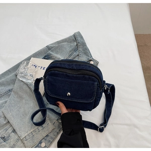 Top view of blue denim crossbody bag with dual zippers and silver snap button pocket