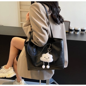 Detail of black textured PU leather tote bag with creative white cloud plush charm