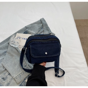 Detail of blue denim crossbody bag with silver buckle and adjustable shoulder strap