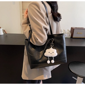 Detail of black leather tote bag with a cute white cloud plush charm in a cozy cafe