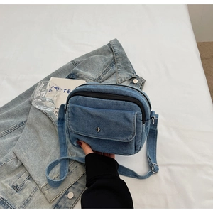 Detail of blue denim crossbody bag with metal snap pocket on soft textile surface