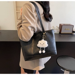 Detail of black faux leather tote bag with white fluffy cloud charm accessory