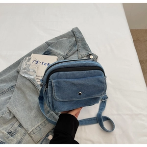 Detail of blue denim crossbody bag with dual zippers and front metal buckle pocket