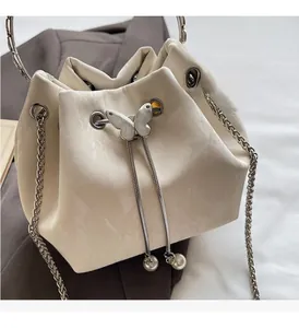 Détail d'un sac seau crème montrant le fermoir papillon argenté et pompons en perles