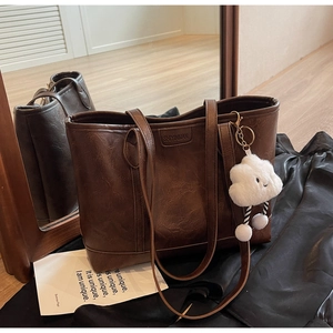 Detail of dark brown vintage tote bag with leather texture and white cloud plush charm