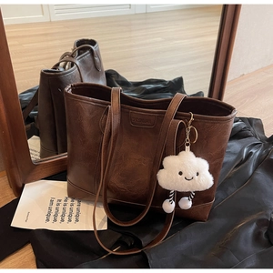 Detail of vintage brown tote bag with leather texture and white cloud plush charm