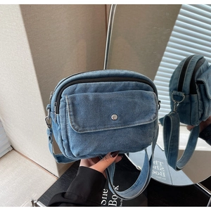 Detail of blue denim crossbody bag featuring zip pocket, metal buckle, and wide strap
