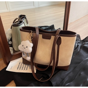 Detail of cream tote bag with brown straps, embossed logo and plush cloud charm