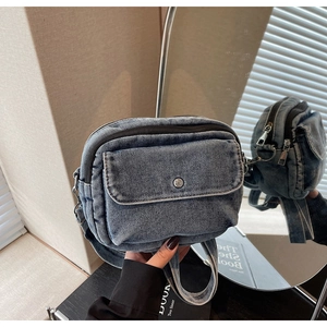 Detail of blue denim crossbody bag with snap pocket and silver metal zipper