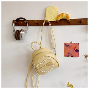 Détail d'un mini sac à dos jaune avec froufrous en dentelle et nœud sur un crochet