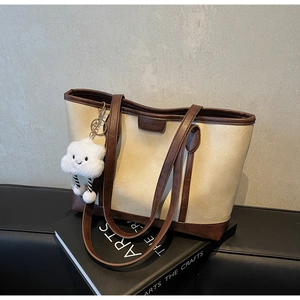 Detail of a contrast tote bag in cream and brown with a plush cloud pendant on a book