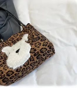 Detail of leopard print tote bag with white plush animal patch and golden metal hardware