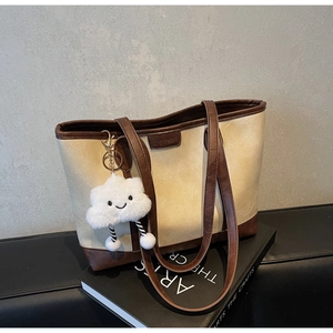 Detail of cream tote bag with contrast brown trim and cute cloud plush charm on art books