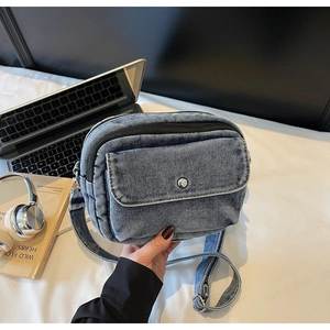 Detailed shot of blue washed denim crossbody bag featuring a front pocket and metal snap