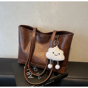 Close-up of brown textured leather tote bag with a creative plush cloud pendant