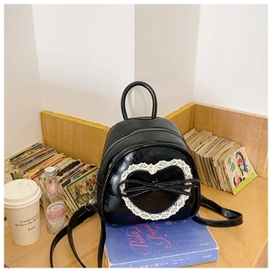 Détail d'un mini sac à dos en cuir noir avec cœur en dentelle blanche et nœud sur étagère