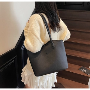 Gros plan d'un cabas noir en cuir grainé avec logo minimaliste porté à l'épaule