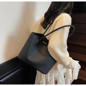 Gros plan sur le grain de cuir litchi noir et le logo discret du sac fourre-tout