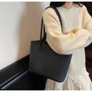 Gros plan d'un sac cabas noir en cuir grainé avec de longues anses porté à l'épaule
