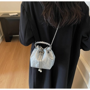 Sac seau argenté avec fermoir papillon et poignée perlée porté par un mannequin