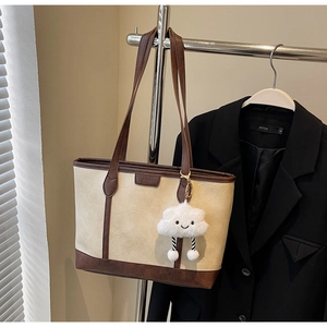 Detail of beige tote bag with brown trim and cute white plush cloud charm hanging