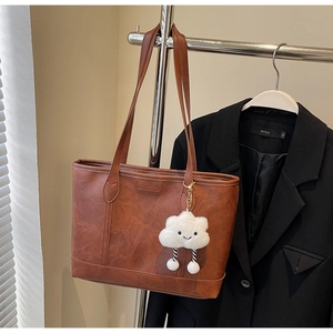 Detail of a brown leather tote bag with SHYVUMAN logo and cloud plush charm