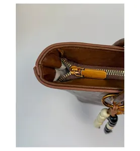 Detail of smooth gold metal zipper and bead pendant on brown leather tote bag