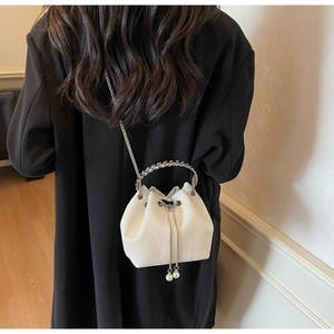 Détail d'un sac seau blanc à cordon avec poignée chaîne argentée et perles élégantes