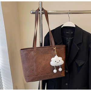 Close-up of brown vintage tote bag with leather texture and white cloud plush charm