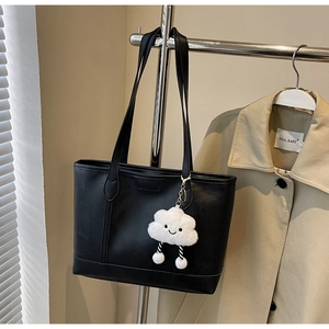 Detail of black faux leather tote bag with a cute smiling cloud plush charm hanging on handle